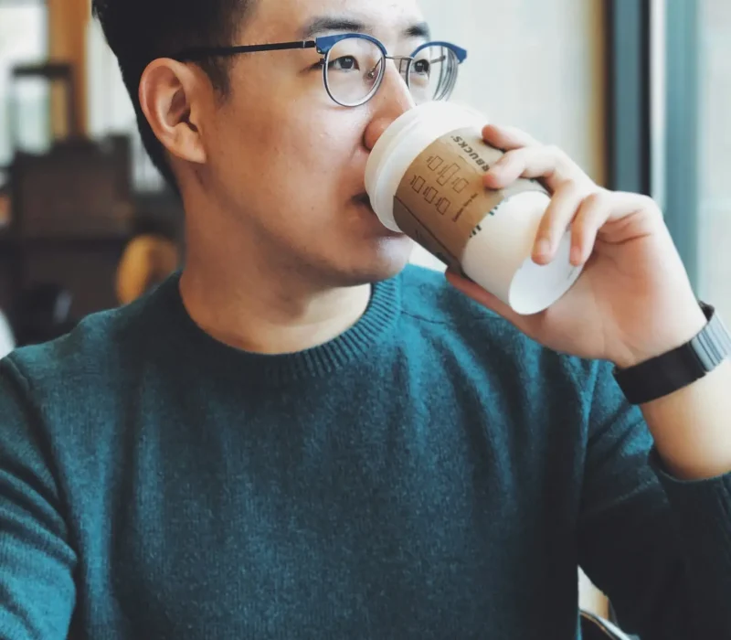 Professional Asian Man Drinking Coffee in Grey sweater at coffee shop. Professional Asian Man Drinking Coffee in Grey sweater at coffee shop.
