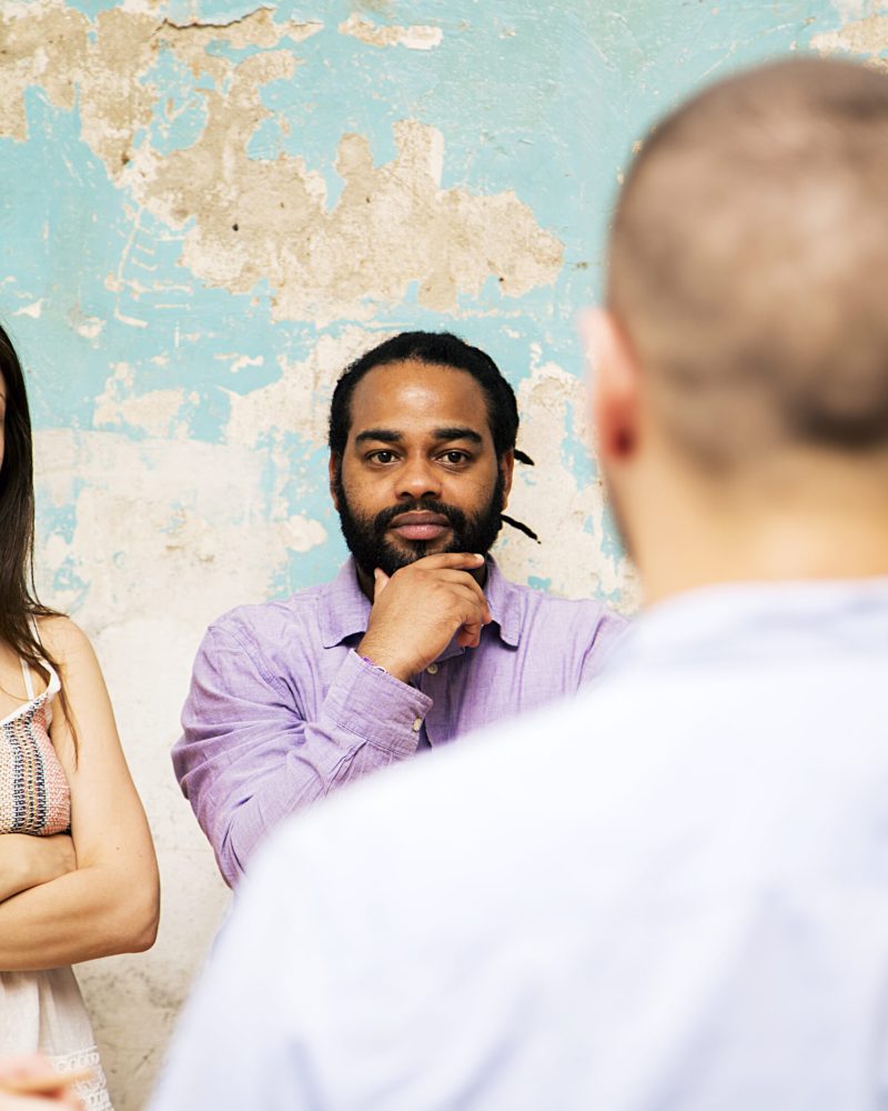 Young man speaks to other young people by grunge wall